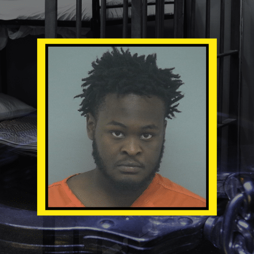 Mugshot of a black man with short dreadlocks, wearing an orange shirt.