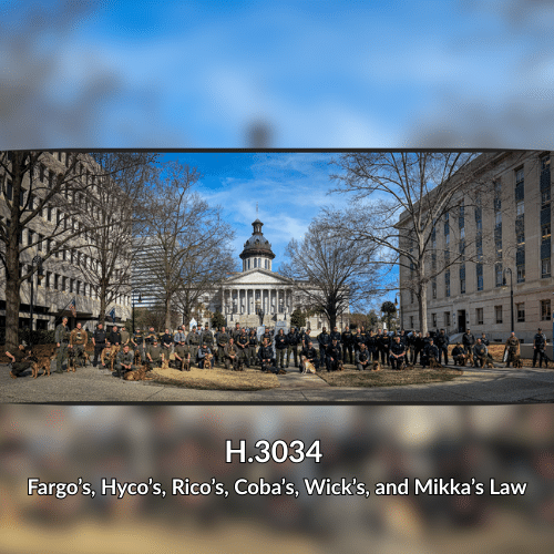 Law enforcement officers and K9s pose for a photo outside of the South Carolina State House in Columbia. A few trees and surrounding buildings are visible under a clear blue sky.
